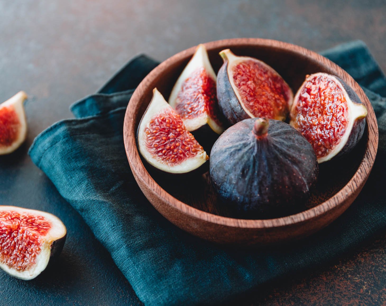 Macro photo of ripe figs in a wooden small bowl on a table.